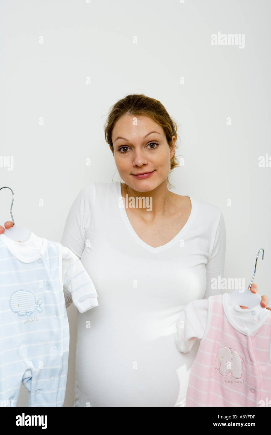 Donna incinta scrollare mantenendo fino blu e rosa abbigliamento bambino Foto Stock