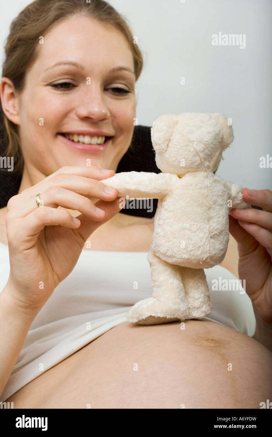 Donna incinta seduta verso il basso e tenendo un orsacchiotto Foto Stock