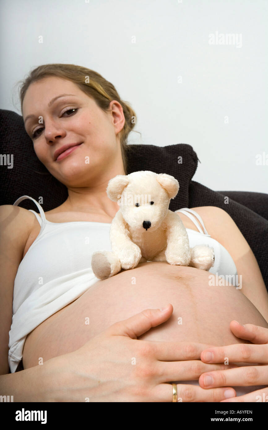 Donna incinta a sedersi con un orsacchiotto sul suo stomaco Foto Stock
