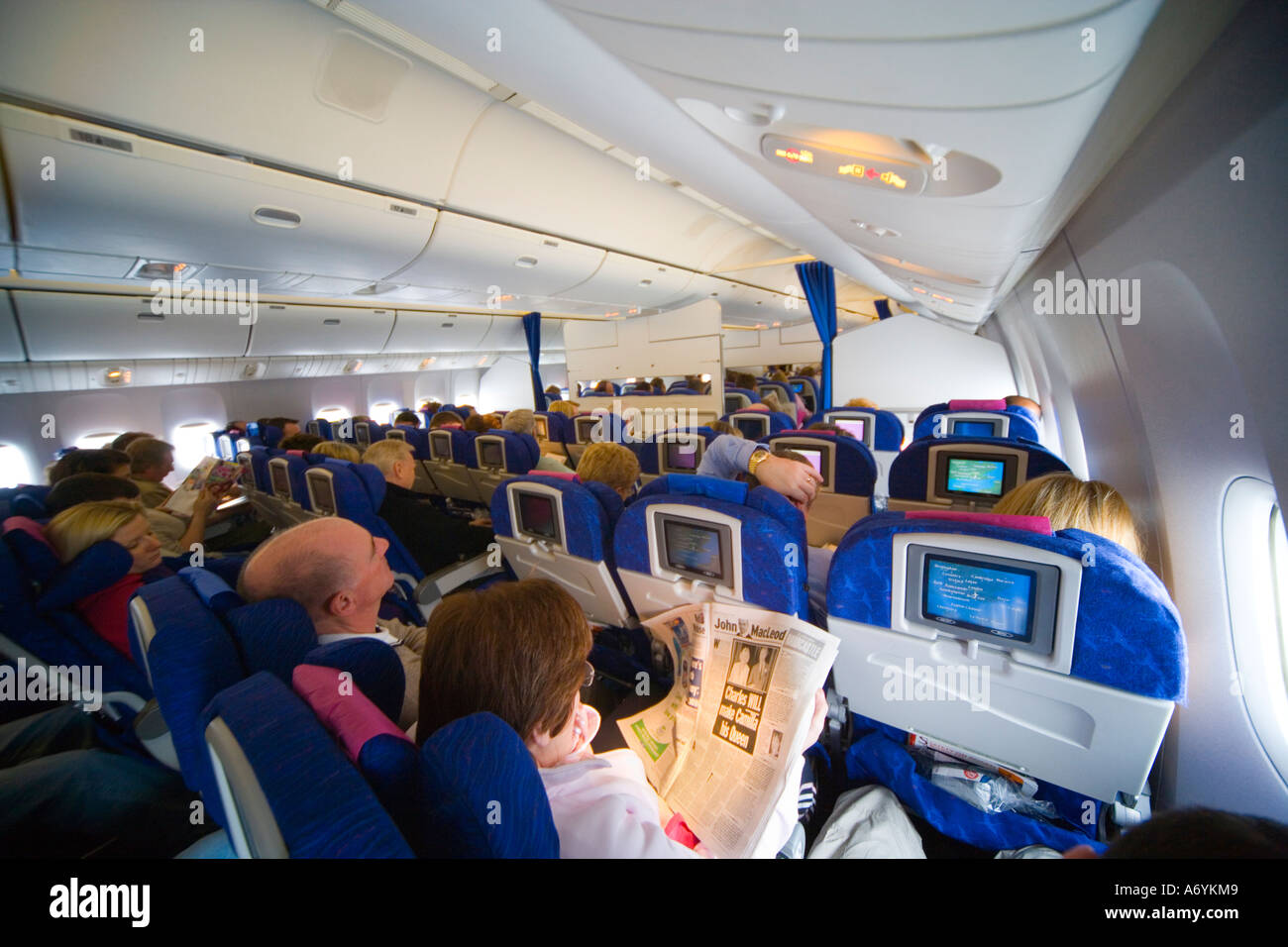 Passeggeri nella affollatissima classe economy cabina su aeromobili Boeing 777 in volo con segnale di allacciare le cinture di sicurezza JMH illuminato1252 Foto Stock