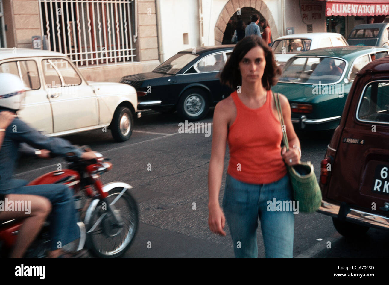 Piuttosto giovane donna in una parte superiore rossa e blu jeans denim attraversando la strada a St Tropez 1974 Foto Stock