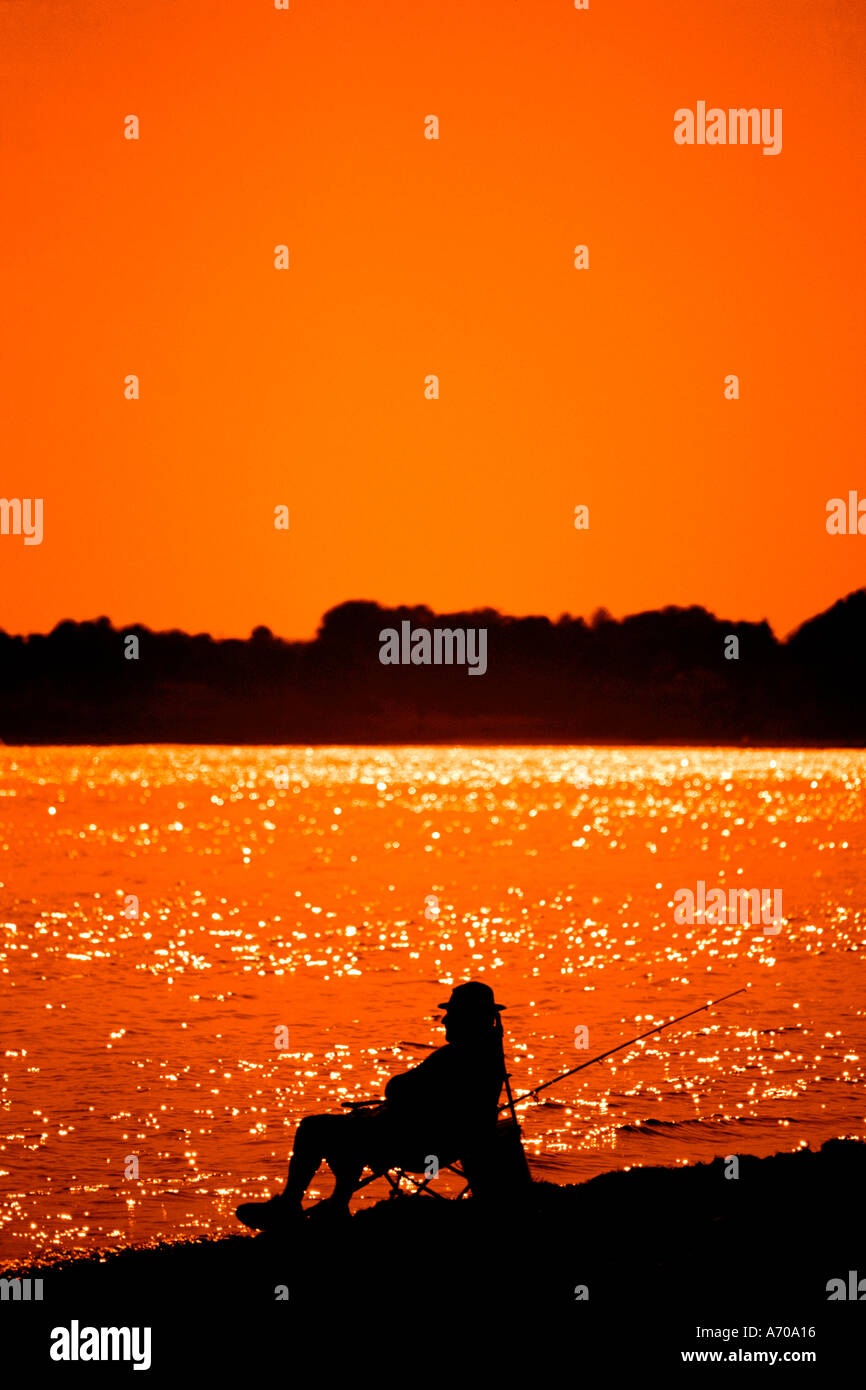 L'immagine verticale della persona seduta in cattedra presso la spiaggia con la canna da pesca al tramonto Foto Stock