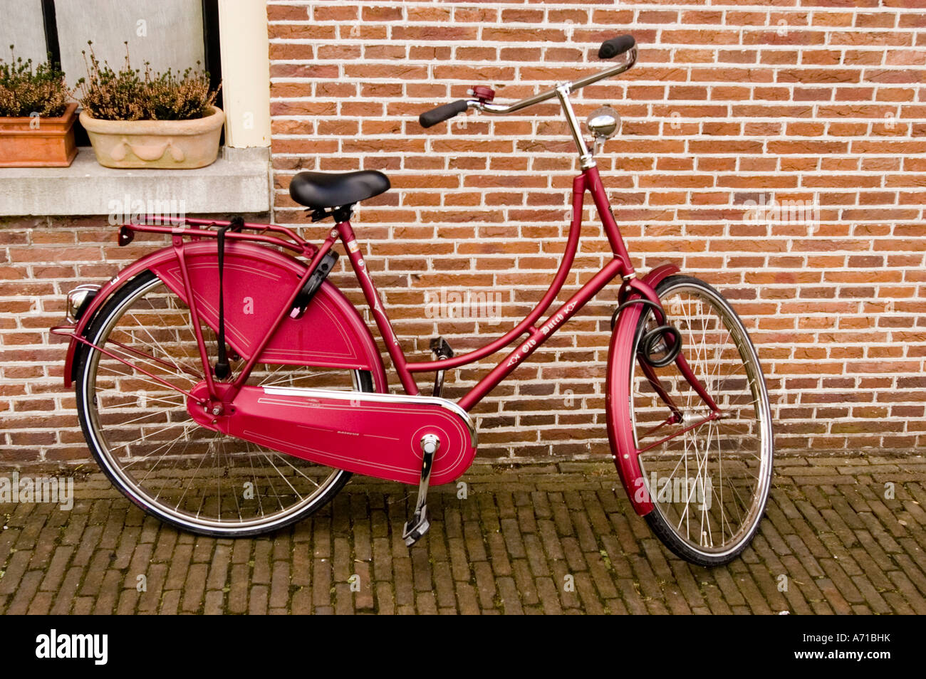 Tipica bicicletta olandese parcheggiata accanto a una casa di mattoni rossi ad Haarlem, nell'Olanda settentrionale. Classica bici da città color marrone su un marciapiede in mattoni. Foto Stock