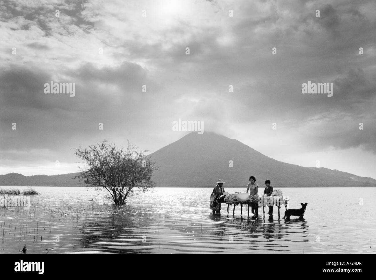 Il lago di Managua, Nicaragua: una famiglia lava i panni nelle acque del lago di Managua mentre vulcano Momitombo effonde il fumo Foto Stock