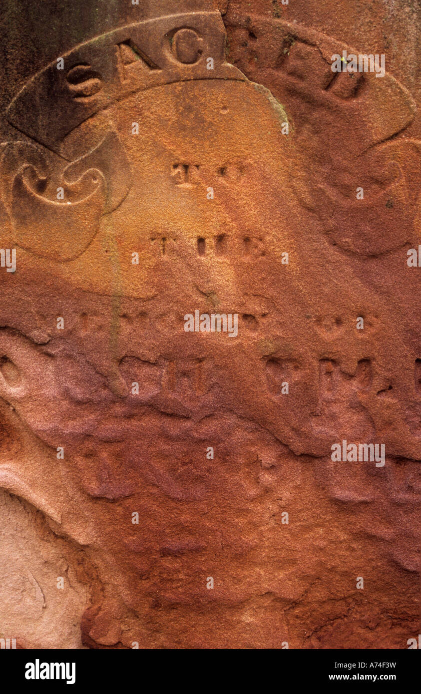 Close up di calda pietra arenaria rossa pietra tombale su cui è appena leggibile sacro alla memoria di con tutte le altre parole eroso Foto Stock