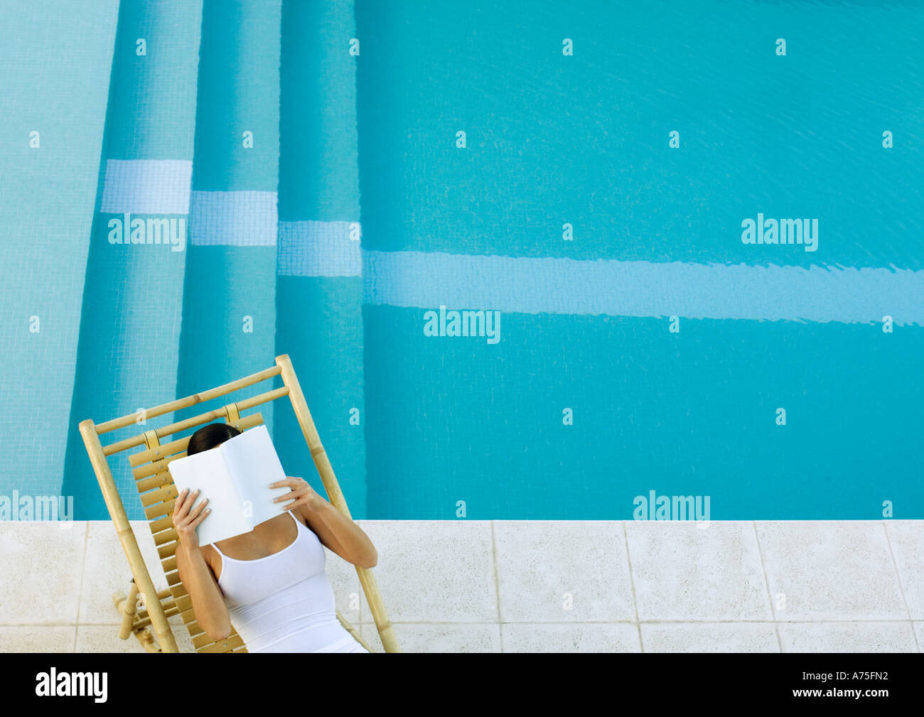 Donna seduta in sedia a sdraio in piscina, lettura, ad alto angolo di visione Foto Stock