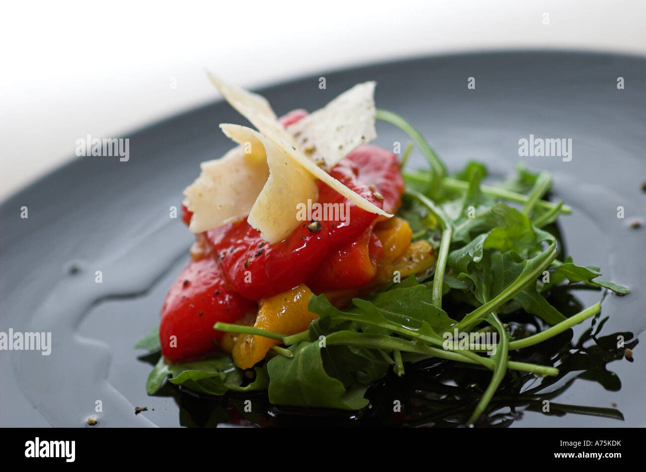 Una selezione di antipasti misti peperoni arrosto su un letto di rucola con scaglie di Parmigiano servito su una piastra nera Foto Stock