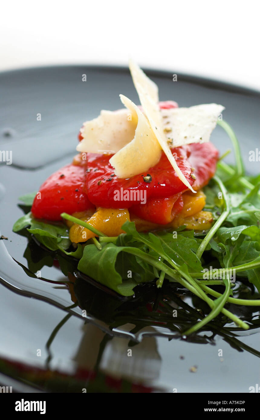 Una selezione di antipasti misti peperoni arrosto su un letto di rucola con scaglie di Parmigiano servito su una piastra nera Foto Stock