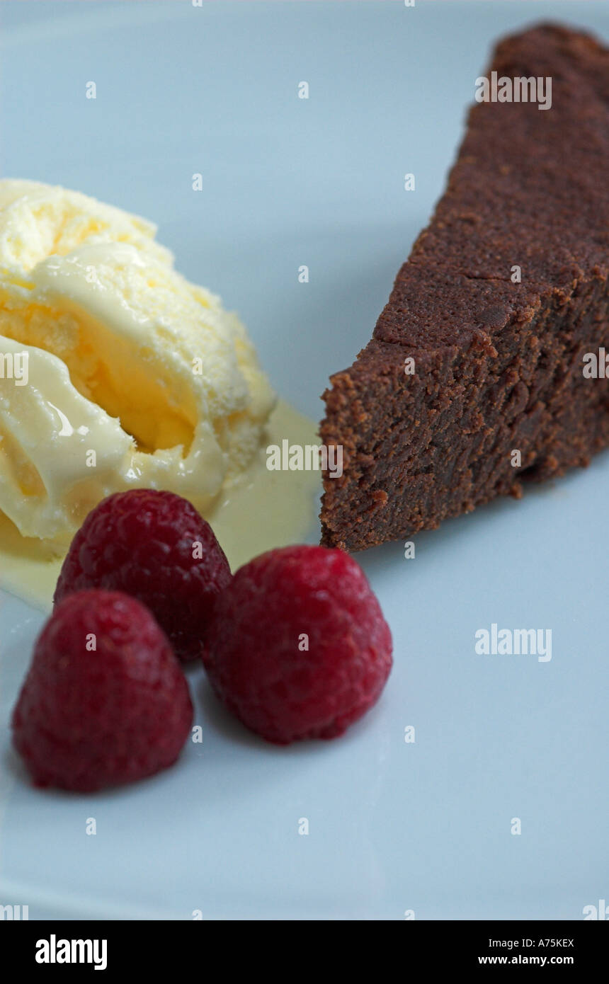 Una fetta di cioccolato fondente torta su un bianco piatto accompagnato da gelato e di lamponi Foto Stock