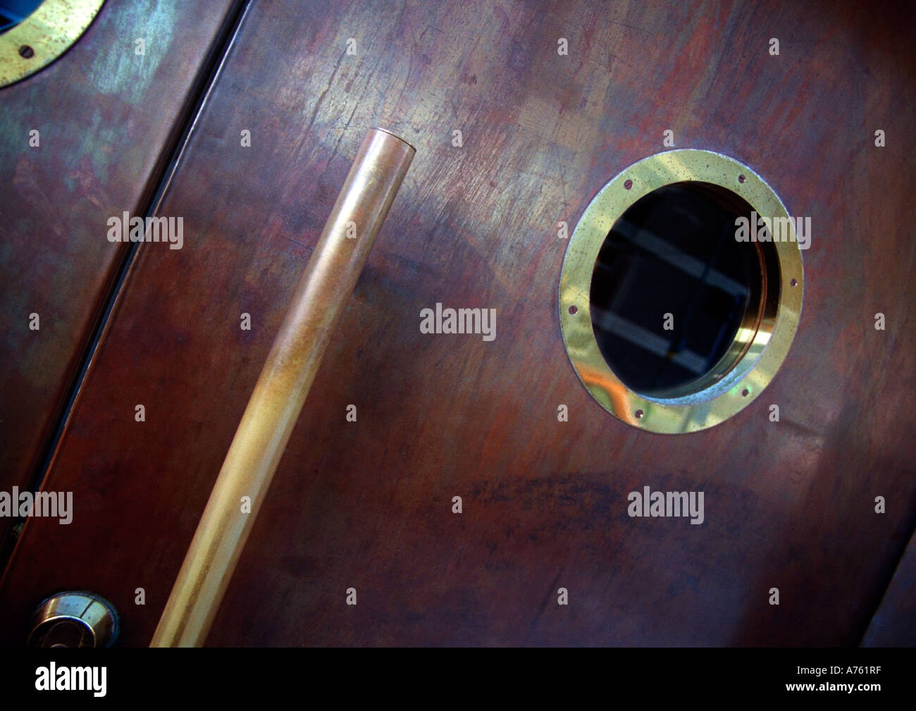 Oblò in ottone e maniglia della porta su una porta di legno Foto Stock