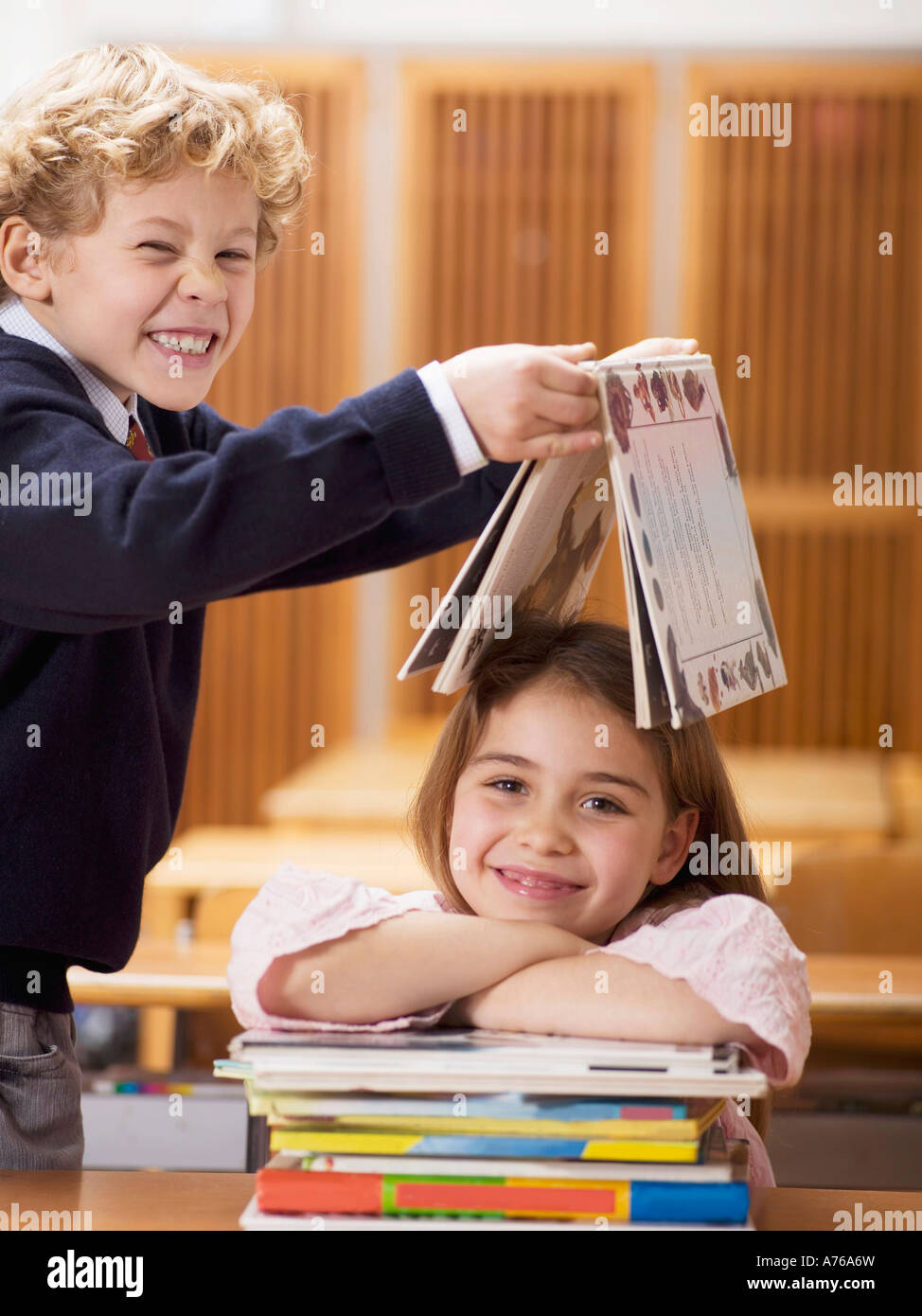 Bambini (4-7) in aula, ragazzo azienda prenota sulla testa della ragazza sorridente Foto Stock