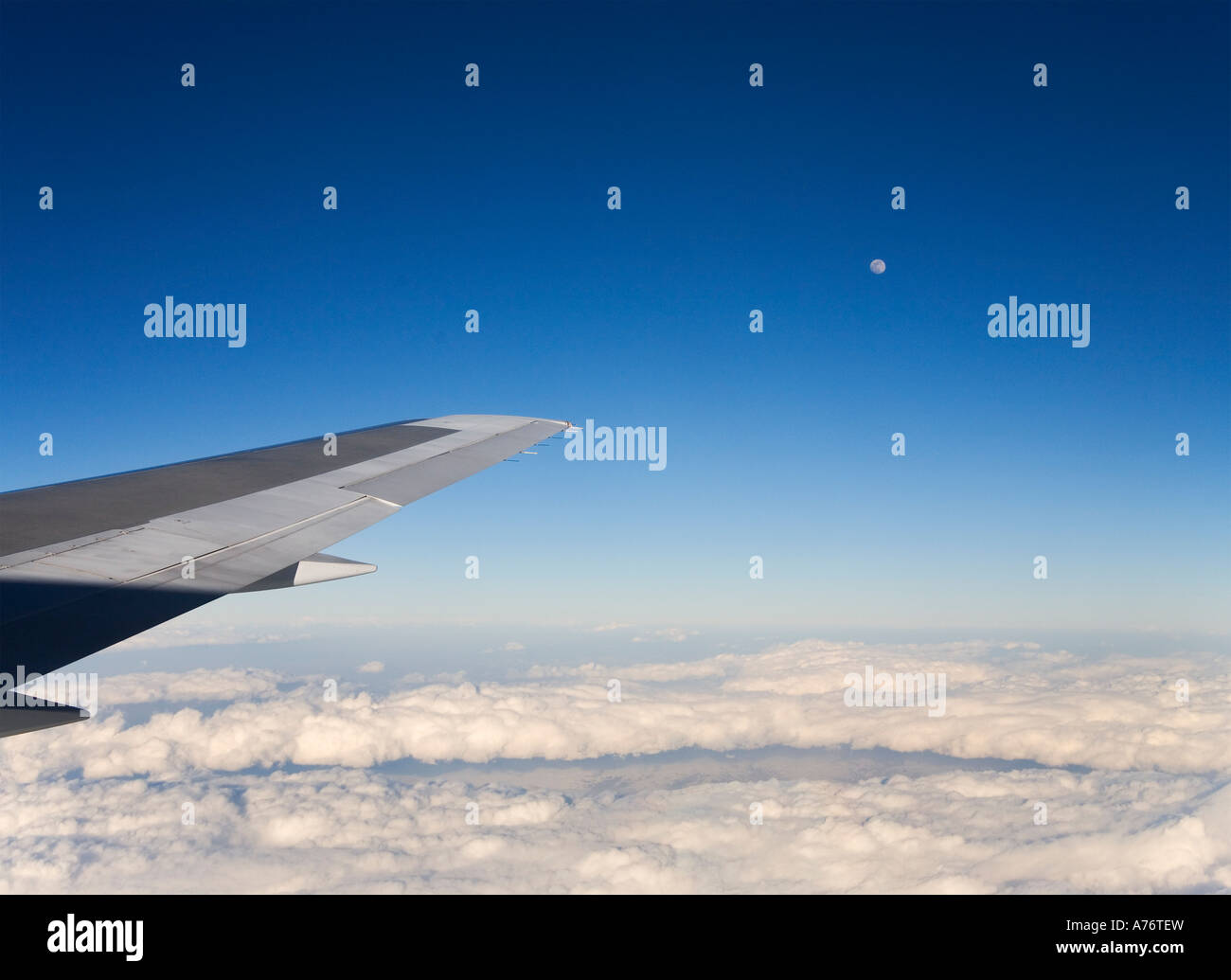 Vista aerea guardando verso il basso sulle nuvole bianche battenti su di loro in alta quota con aeromobili ala punta contro il cielo blu e la luna piena Foto Stock