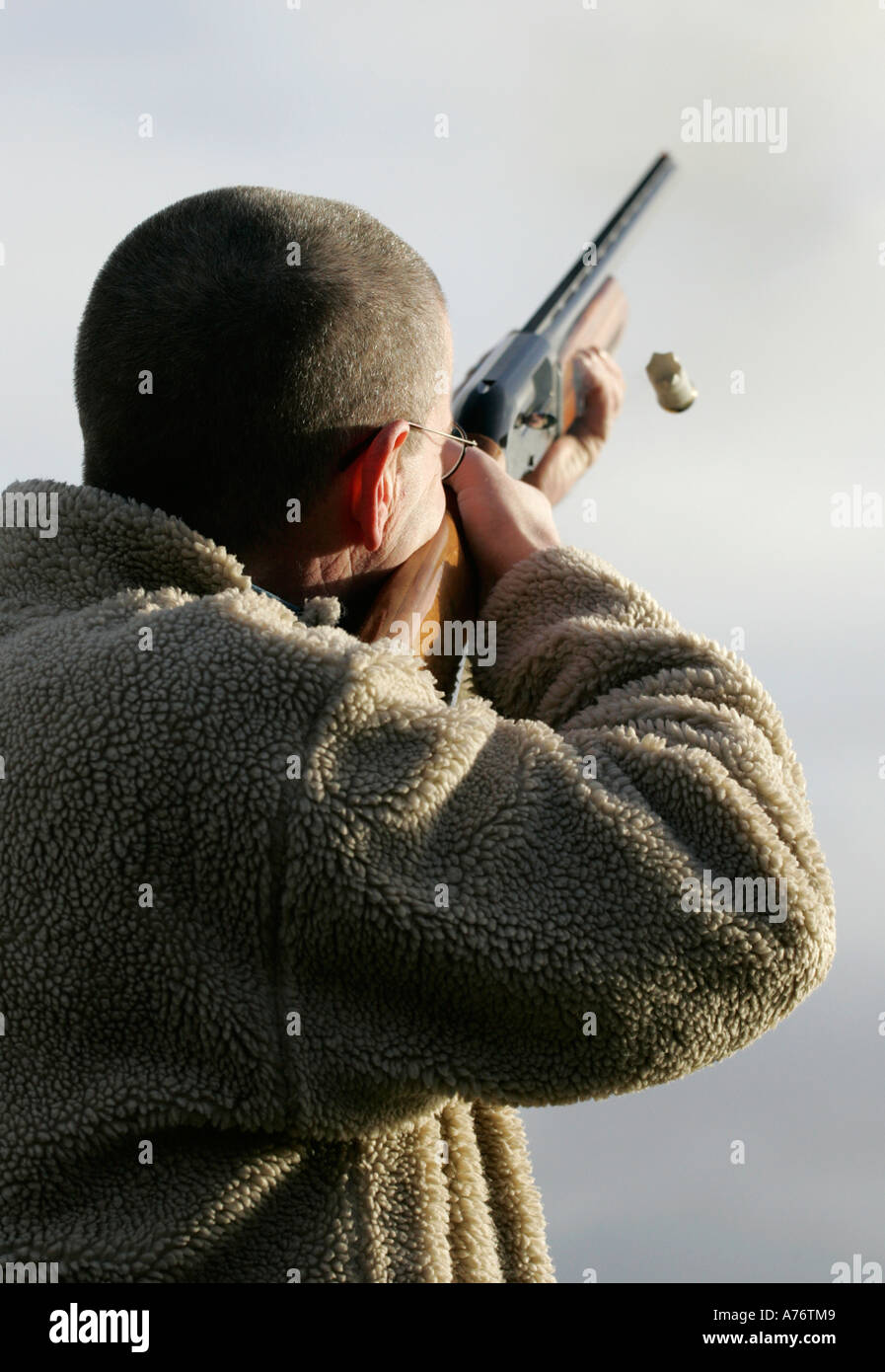 Uomo con occhiali in giacca in pile fucile da caccia di sparo in cielo con espulsione della cartuccia su dicembre giornata di riprese nella contea di Antrim Foto Stock
