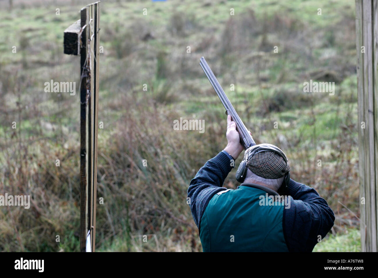 Uomo in Abbigliamento da caccia e gli otoprotettori prende la mira con un fucile in stand di tiro su dicembre giornata di riprese nella contea di Antrim Foto Stock
