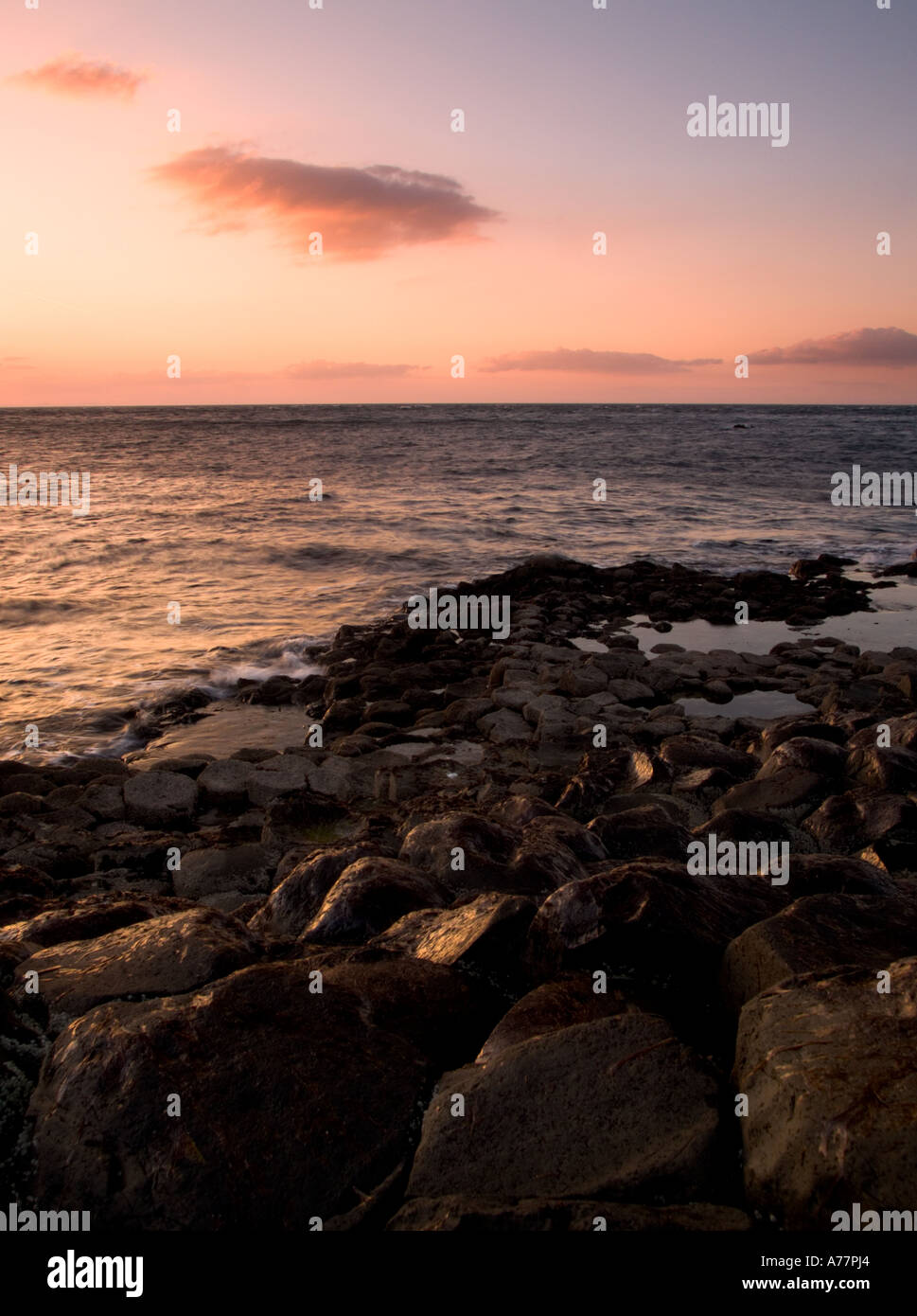 Un bel golden glow scende sulle rocce dei Giganti Causeway Irlanda del Nord come il sole tramonta su un oceano di calma Foto Stock