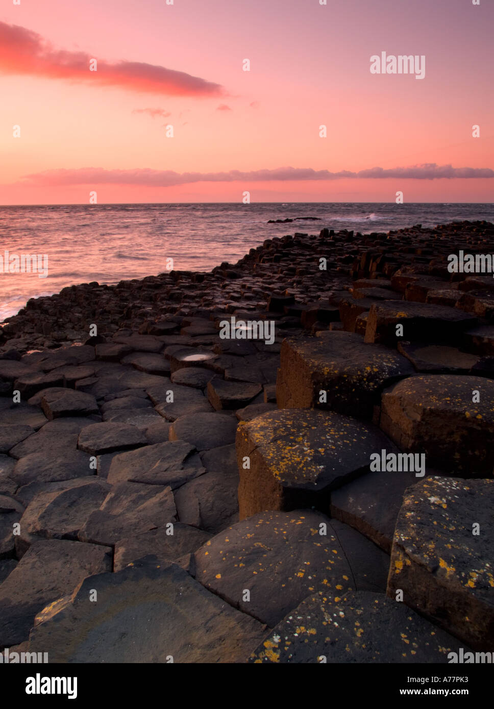 Una bella rosa glow scende sulle rocce dei Giganti Causeway Irlanda del Nord come il sole tramonta su un oceano di calma Foto Stock