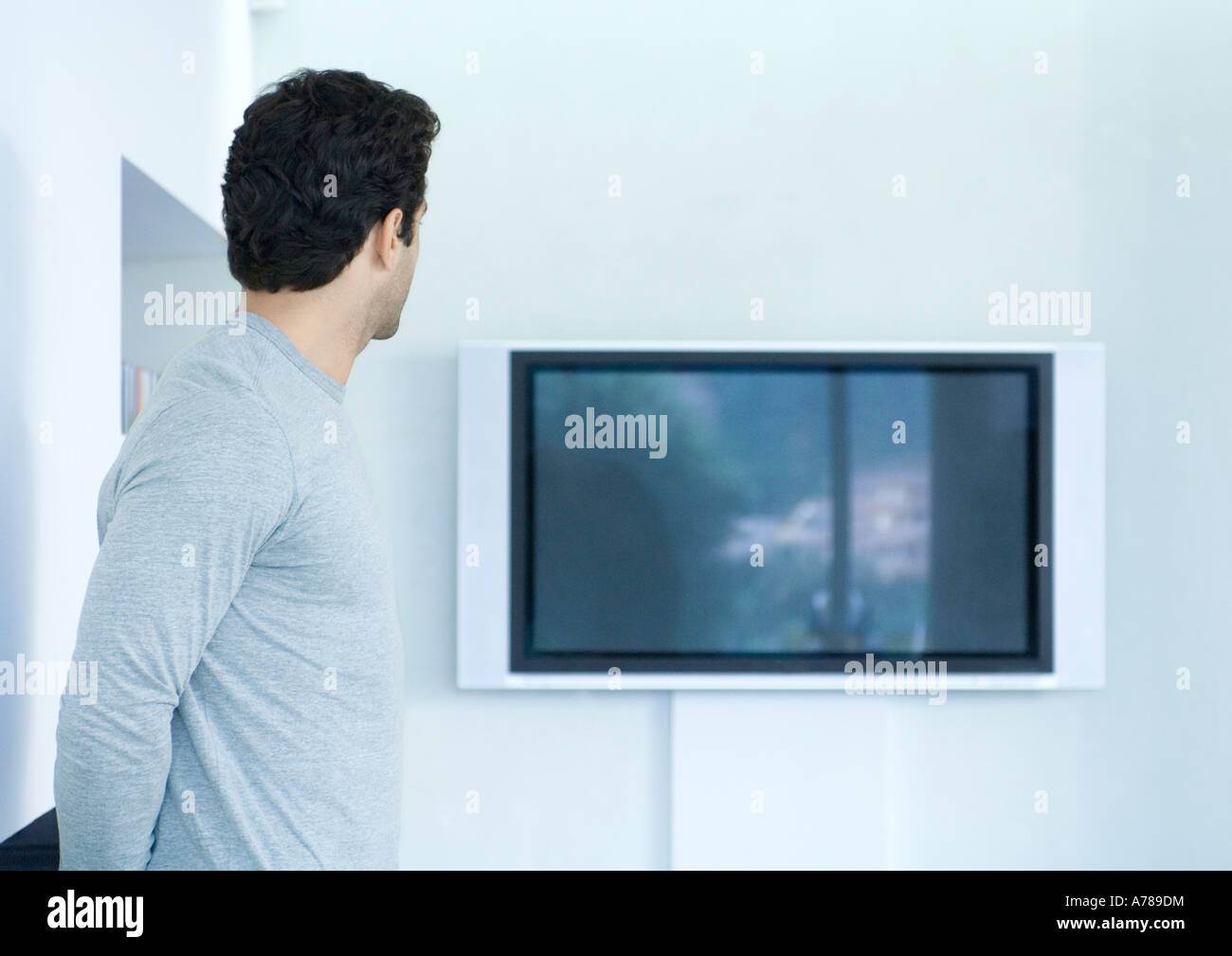 Uomo che guarda verso la tv a schermo piatto a parete Foto Stock