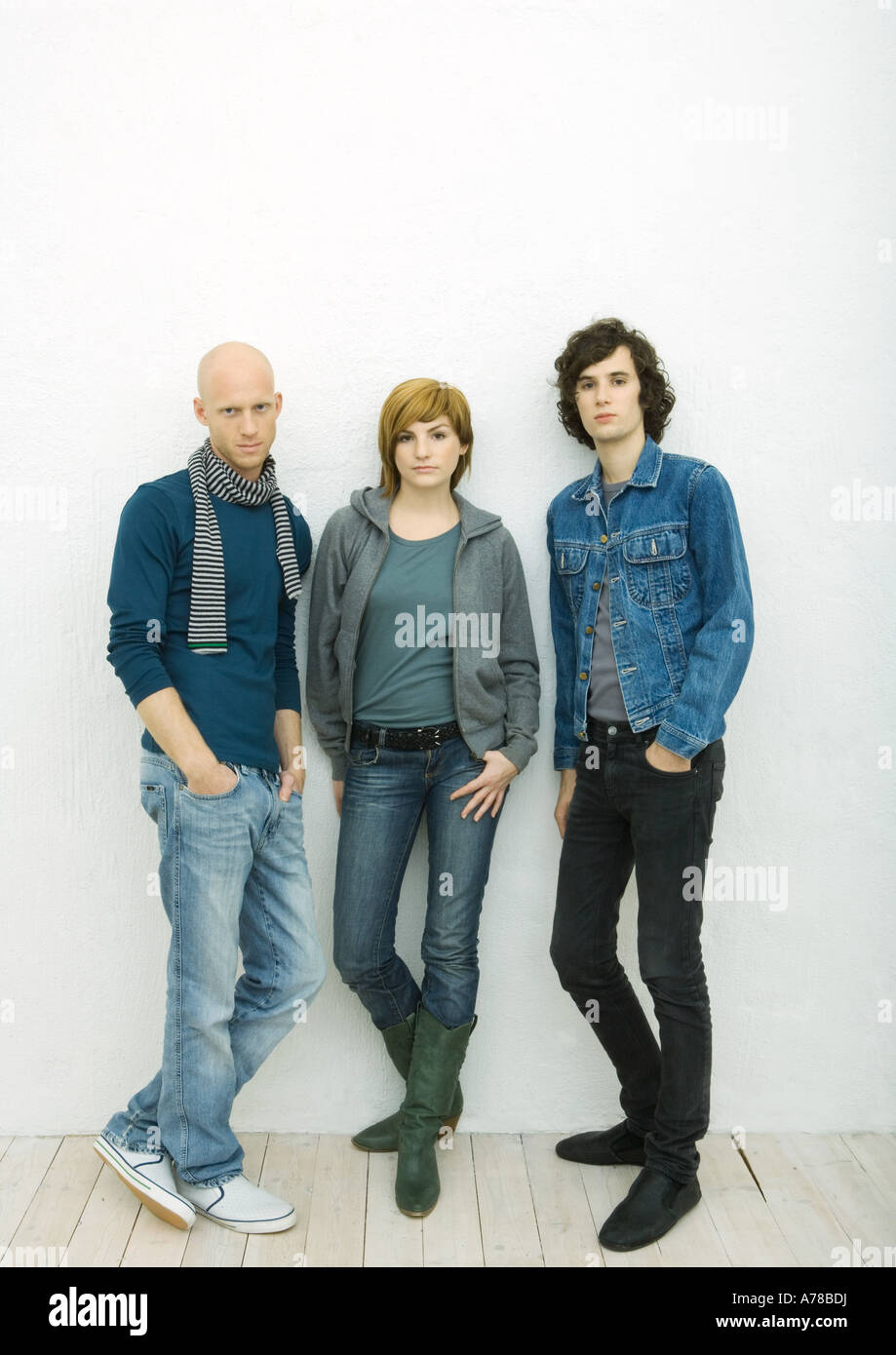 Tre giovani adulti appoggiata contro la parete, guardando la fotocamera a piena lunghezza ritratto, sfondo bianco Foto Stock