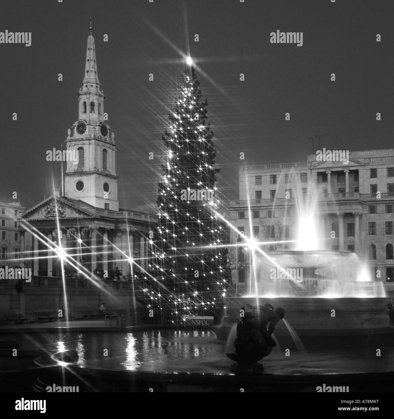 Funzione di acqua in Trafalgar Square Londra Inghilterra REGNO UNITO & albero di Natale luci con proiettori su fontane & St Martin nei campi chiesa & guglia Foto Stock