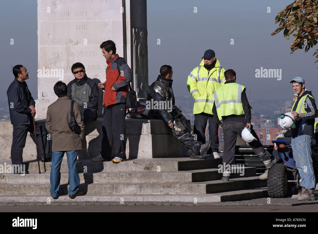 BOYS' parlare. I turisti giapponesi e inglese operai godono di una soleggiata giornata autunnale dalla canadese un monumento nel parco di Greenwich. Foto Stock