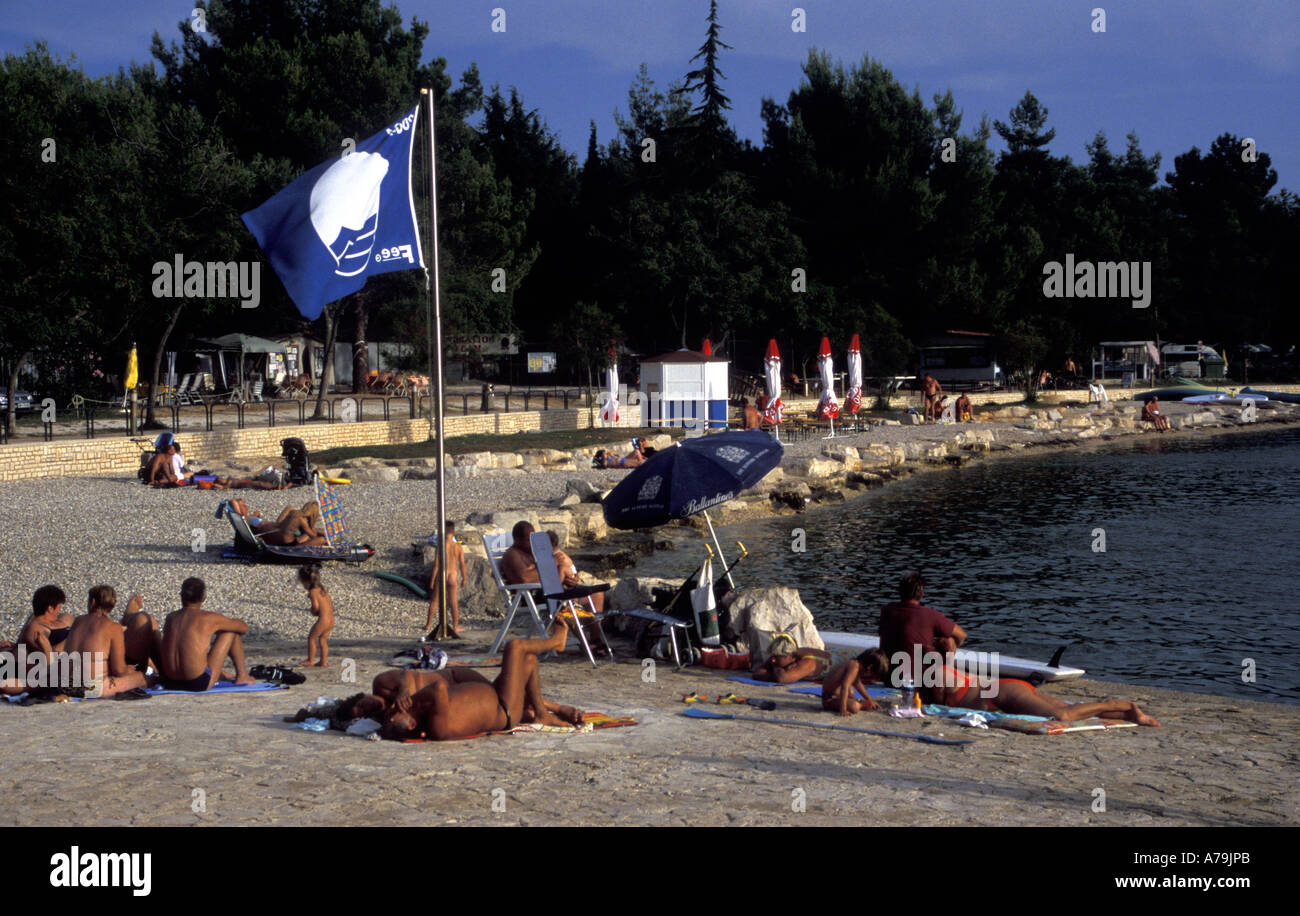 I turisti la concia nel tardo pomeriggio di sole in spiaggia con Bandiera Blu, Istria, Croazia Foto Stock