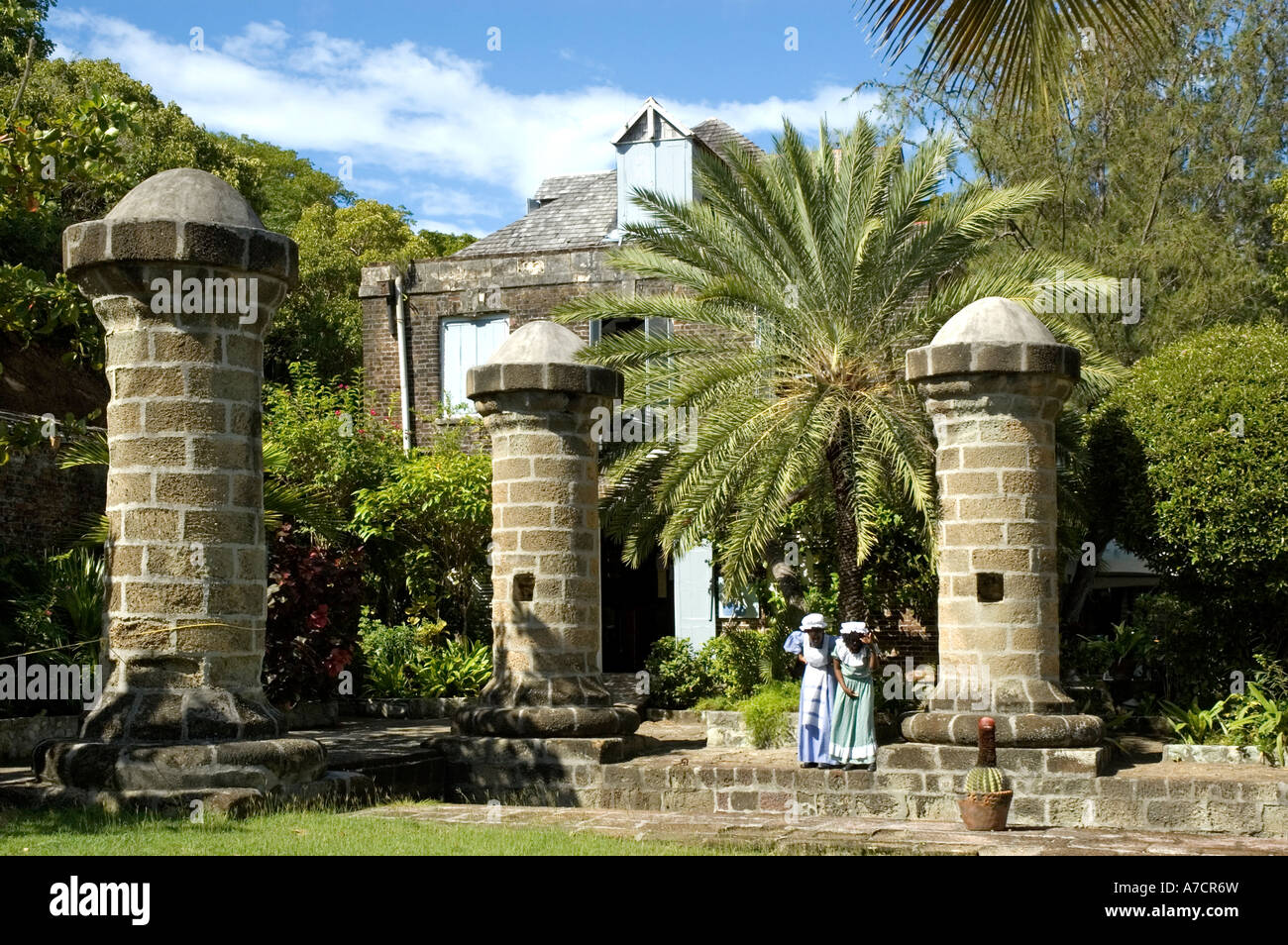 Due locali guide femmina nel XVII secolo abiti in stand by il boat house e veleria pilastri, Nelson's Dockyard, Antigua Foto Stock