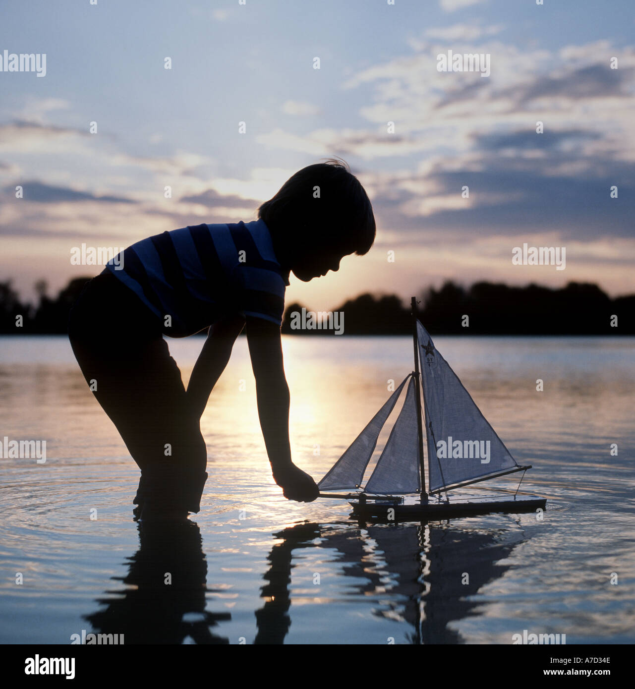 Giovane ragazzo giocando con il giocattolo in barca a vela al tramonto Foto Stock