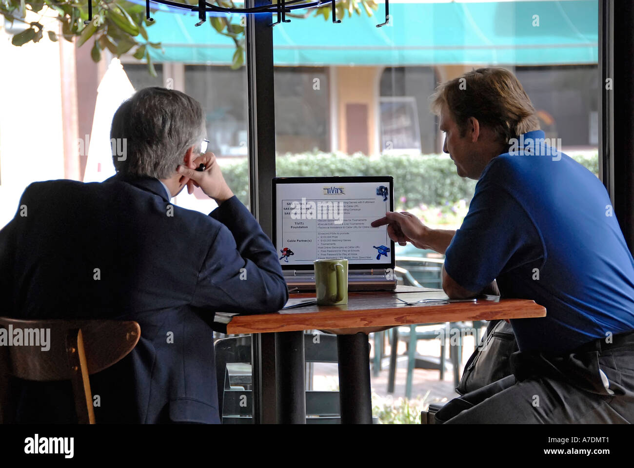 Due uomini di affari professionale condotta soddisfare con un computer portatile come un aiuto in un ristorante durante l'ora di pranzo Foto Stock