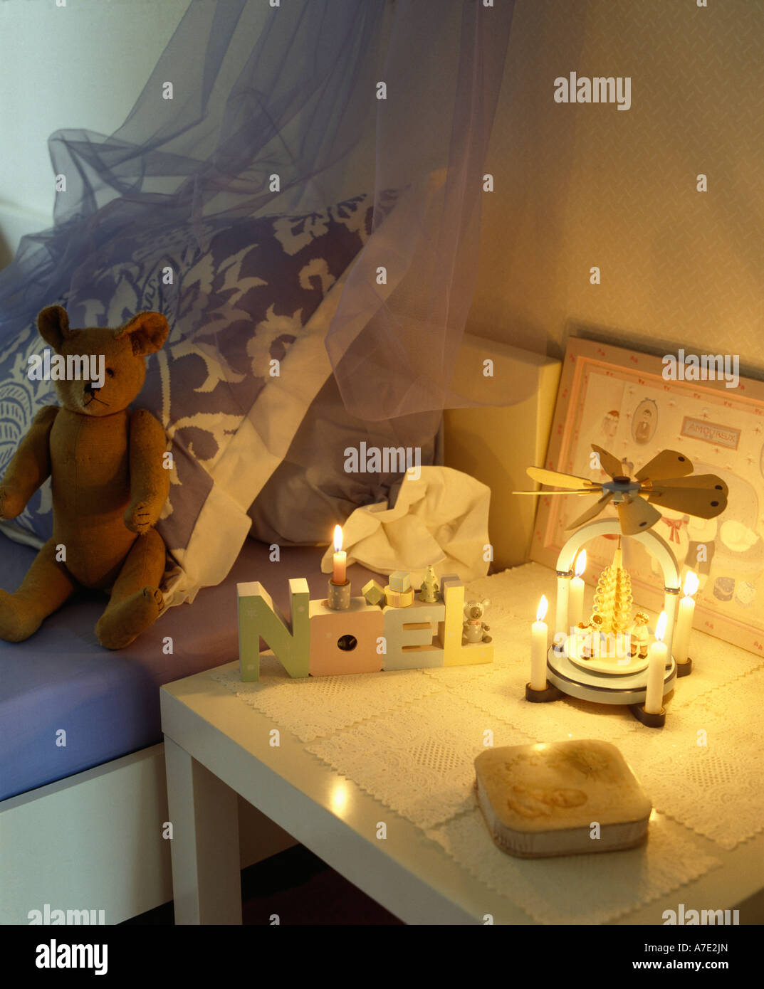 Natale in legno Noel portacandele con candele accese sul tavolo accanto a letto per bambino con Teddy bear Foto Stock