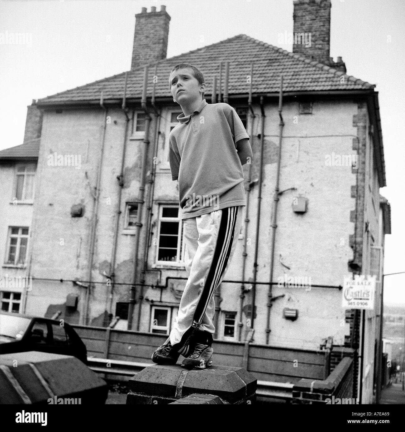 Un giovane ragazzo in piedi su un muro vicino a casa sua in una corsa verso il basso l'alloggiamento station wagon, Clapton, Londra, Regno Unito. Foto Stock