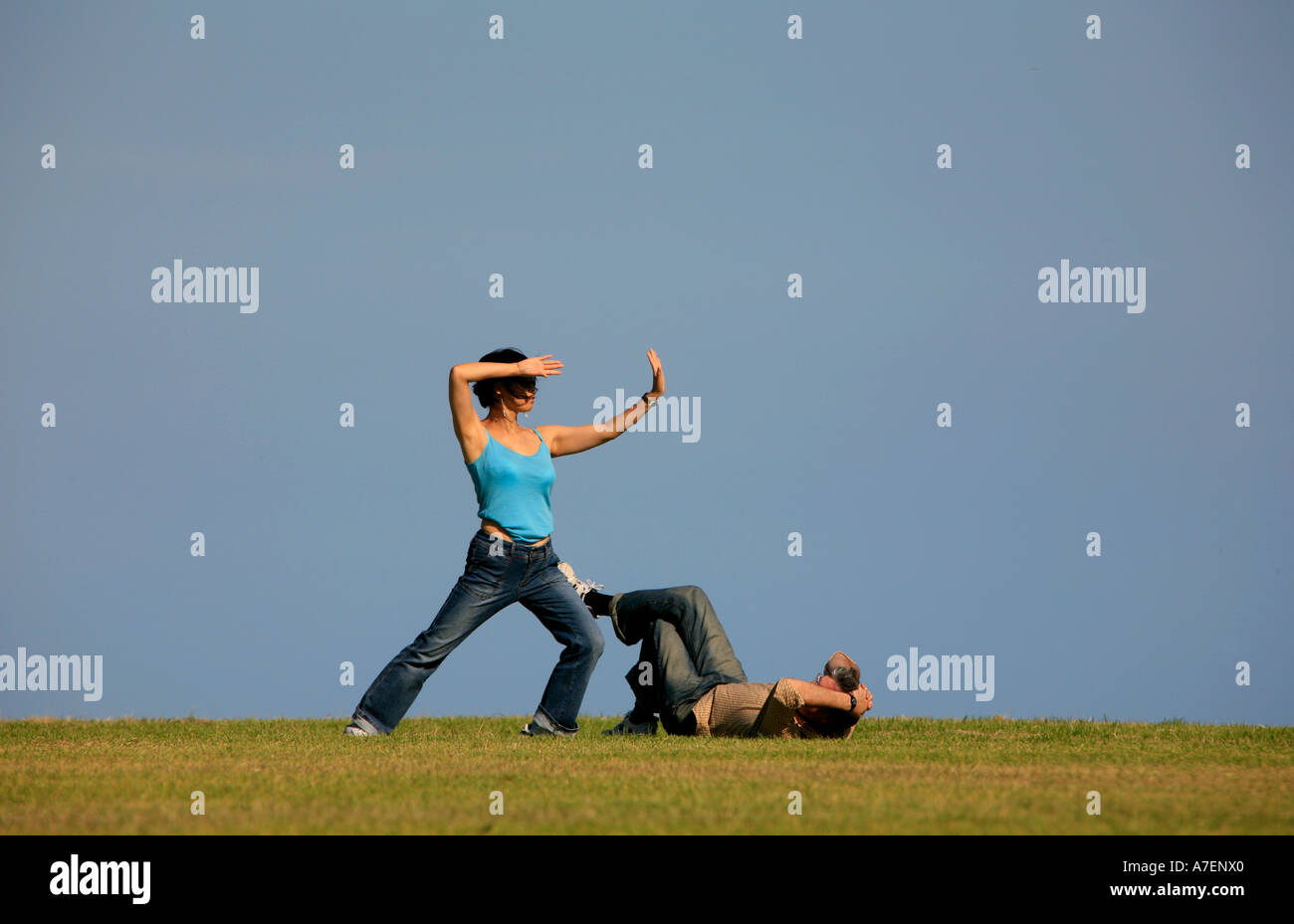 Una donna non Tai Chi mentre il suo partner si stende su erba a guardare Foto Stock