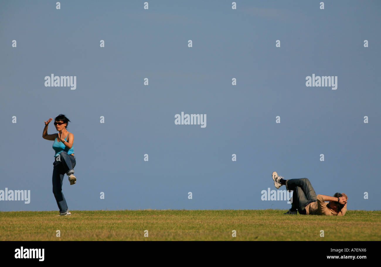 Una donna pratica l'antica arte cinese del Tai Chi mentre il suo partner si stende su erba a guardare Foto Stock