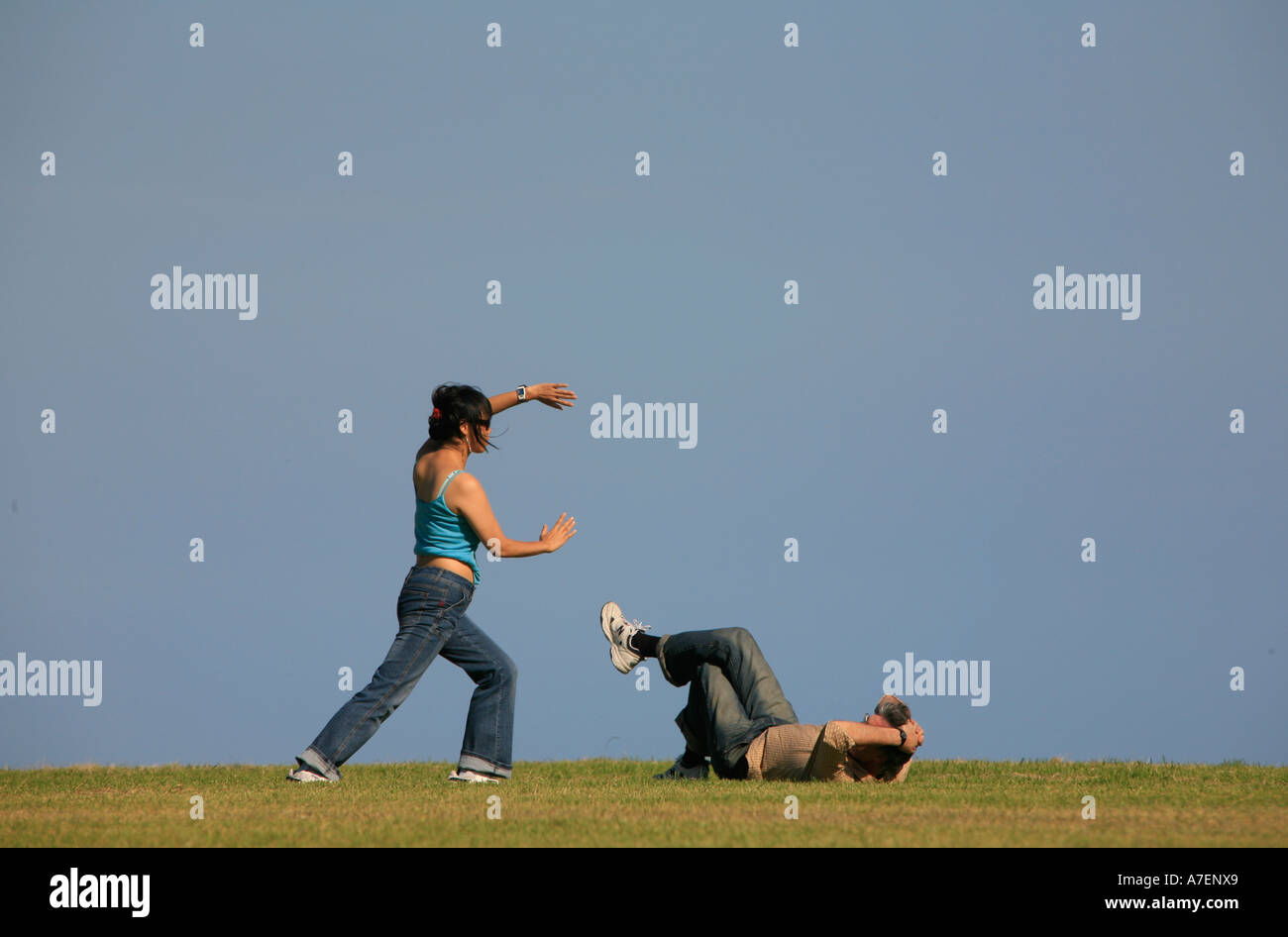 Una donna pratica l'antica arte cinese del Tai Chi mentre il suo partner si stende su erba a guardare Foto Stock