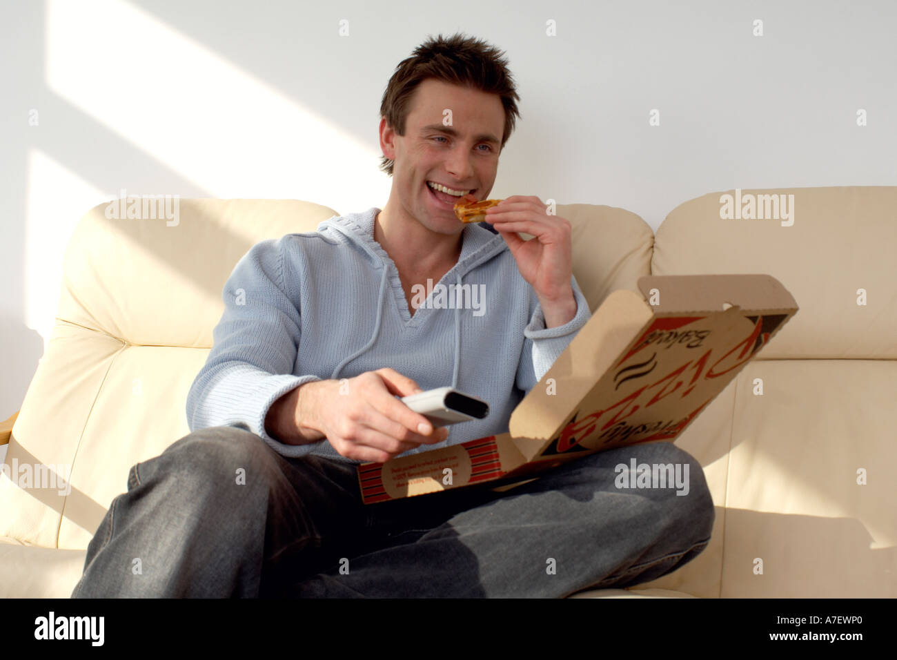 Uomo seduto su un divano a mangiare la pizza e guardare la televisione Foto Stock