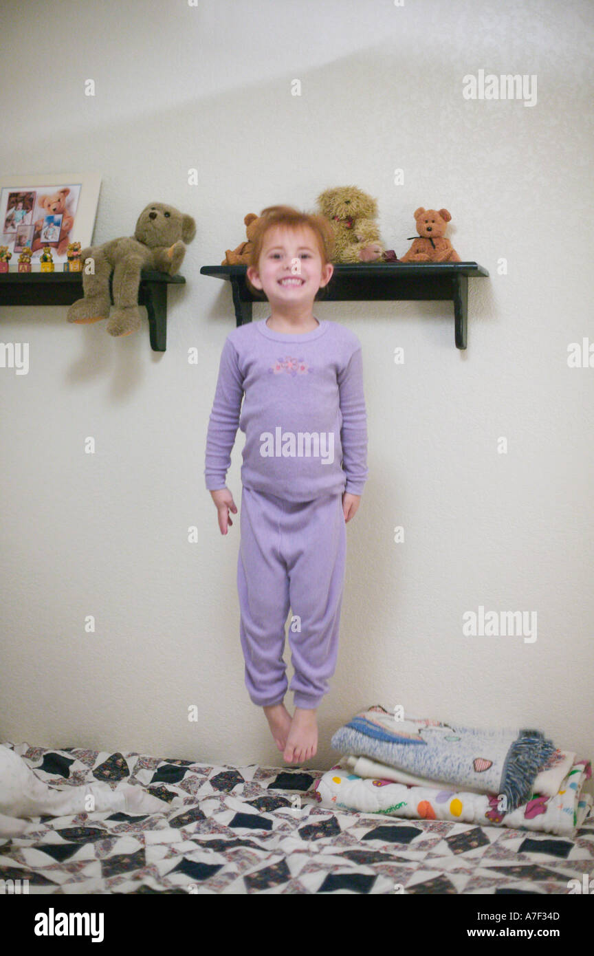 Testa rossa ragazza indossando pigiami e saltare sul letto in camera da letto Foto Stock