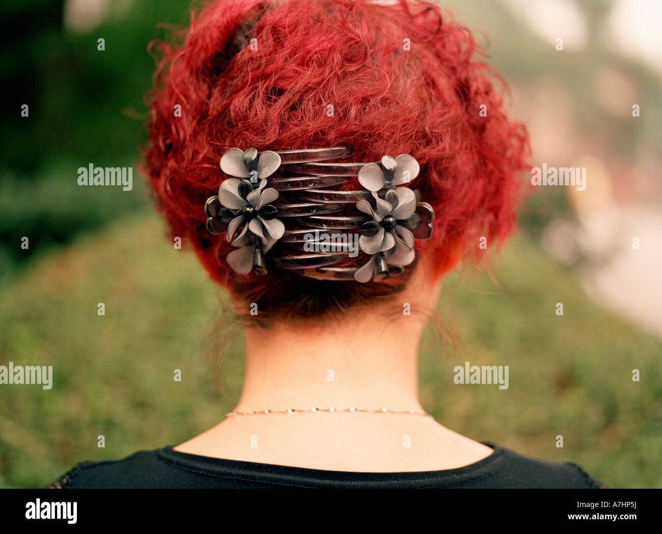 Un ritratto della parte posteriore di una donna cinese s testa con luminosi capelli rossi e grandi fascette che tengono in posizione in un parco Foto Stock