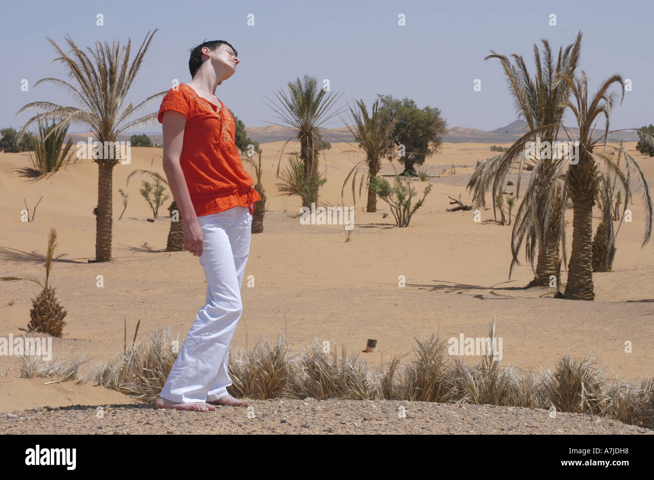 Un giovane turista femminile a piedi nudi nel deserto con le palme che crescono in sabbia e colline in background Foto Stock