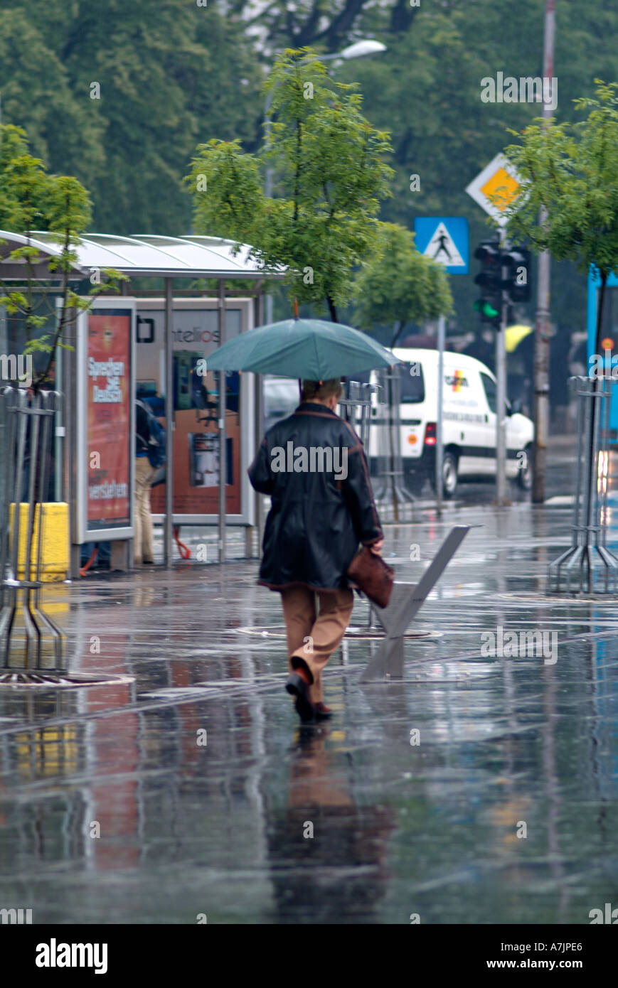 Passeggiate pedonali lungo un marciapiede della città sotto un ombrello durante una doccia a pioggia Foto Stock