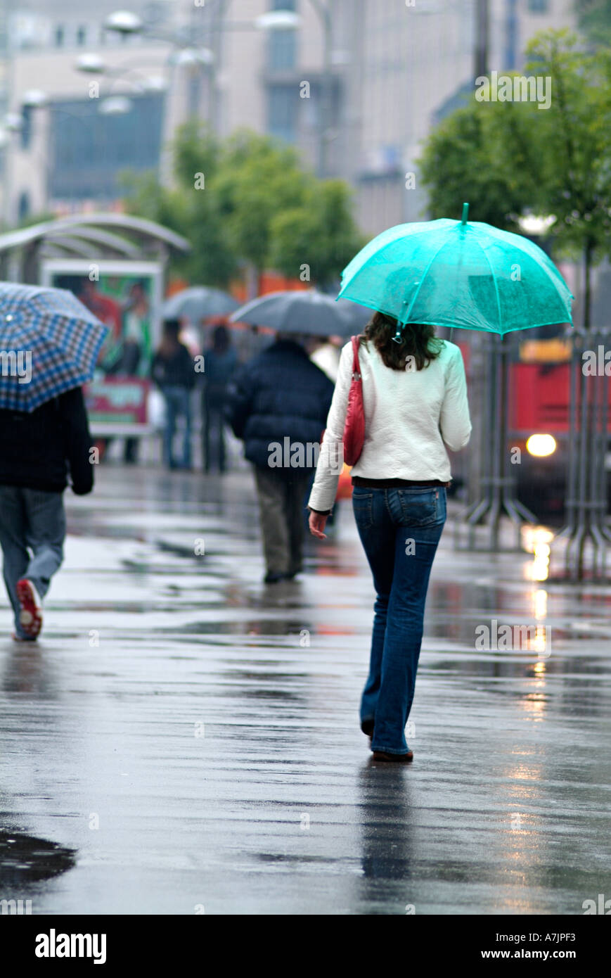 Giovane donna camminare lungo una strada trafficata sotto la pioggia Foto Stock