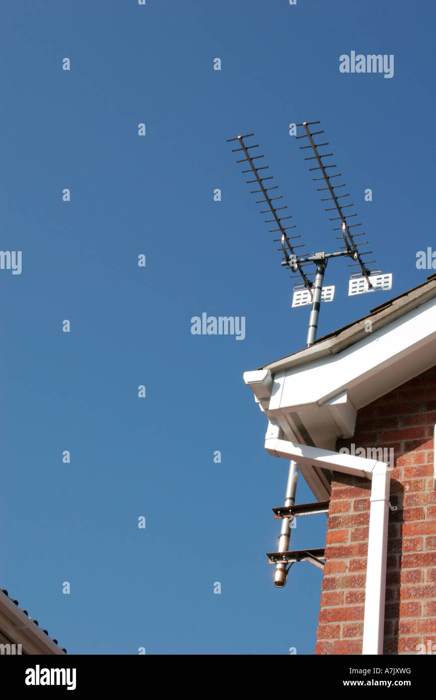 Antenna TV fissata al tetto di una casa in mattoni sotto un cielo estivo azzurro. Foto Stock