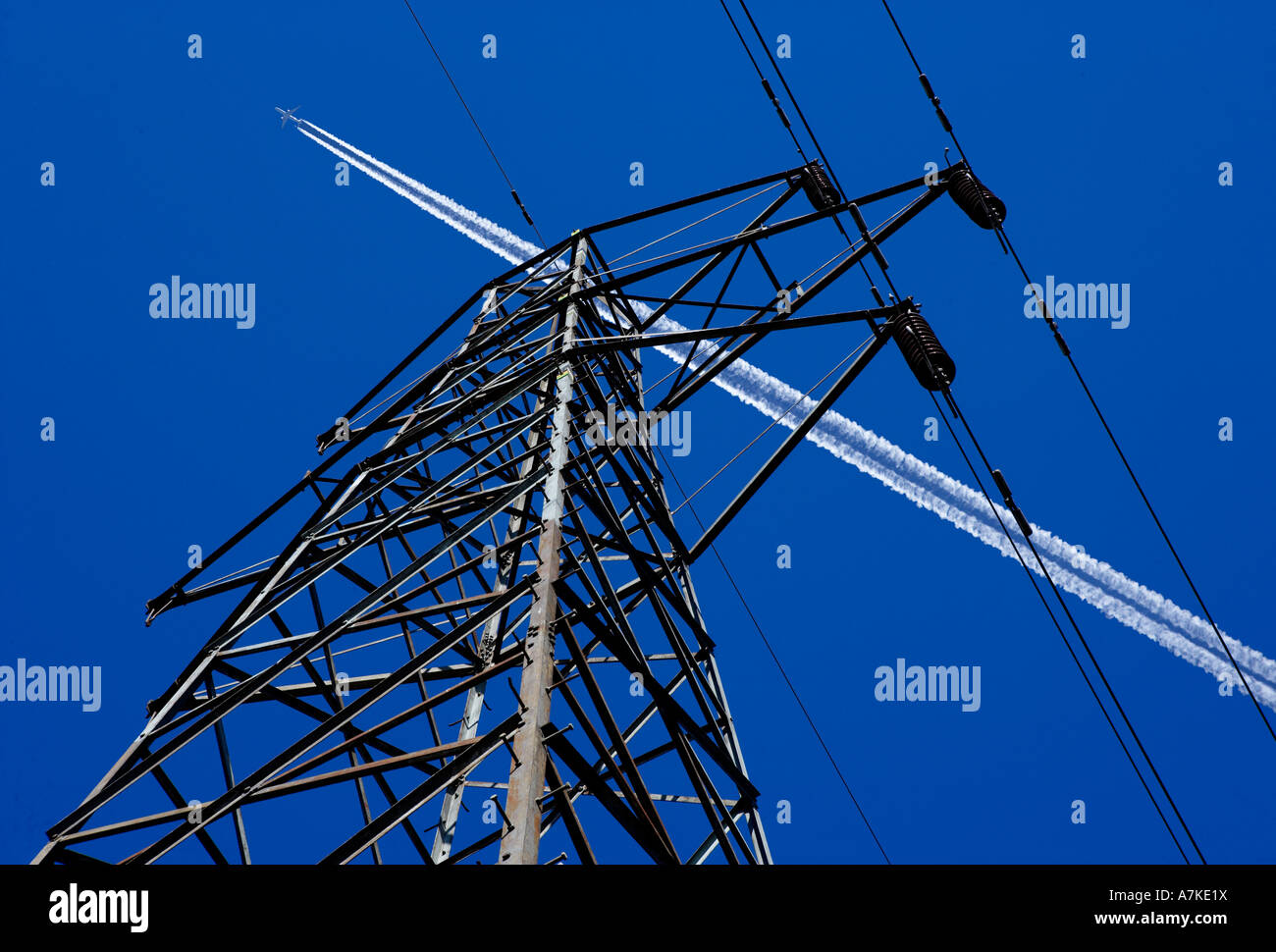 Pilone di elettricità e i cavi con un aeromobile jet sentiero di scarico nel cielo blu Foto Stock