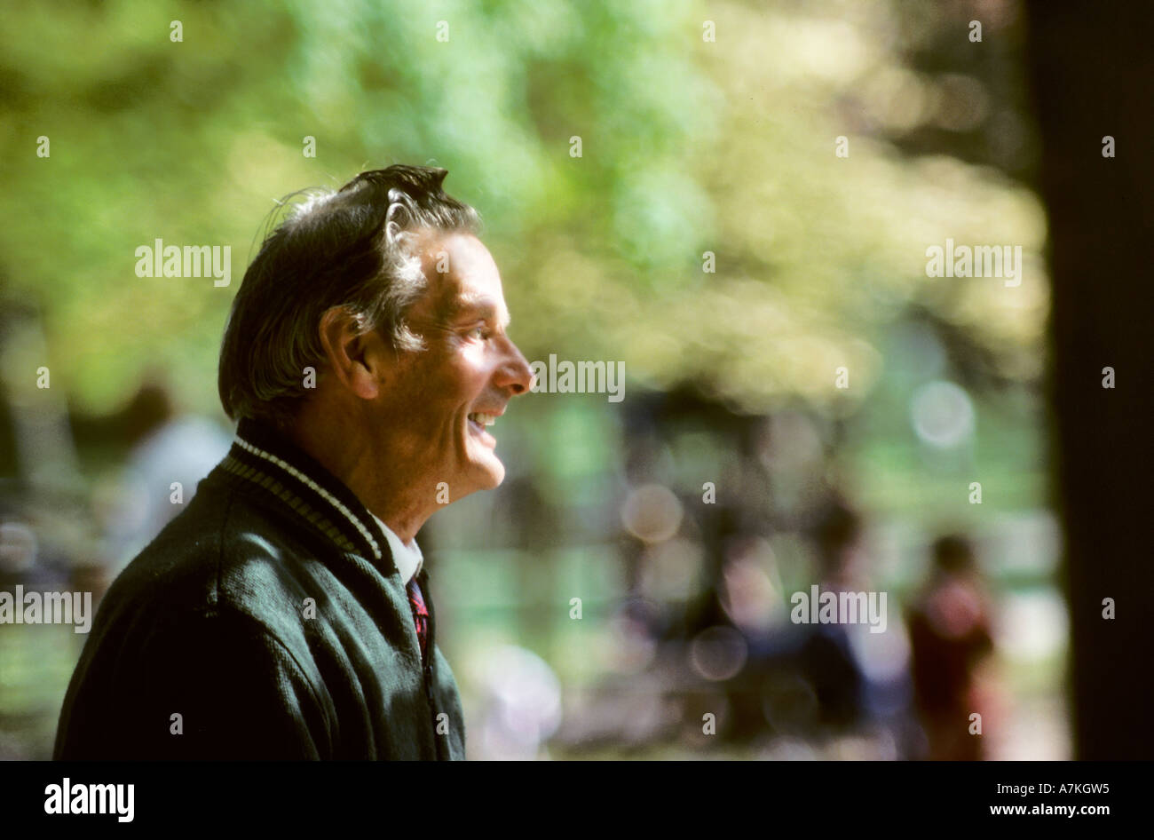 Backlit uomo sorridente contro al di fuori della messa a fuoco lo sfondo in un parco Wales UK Foto Stock