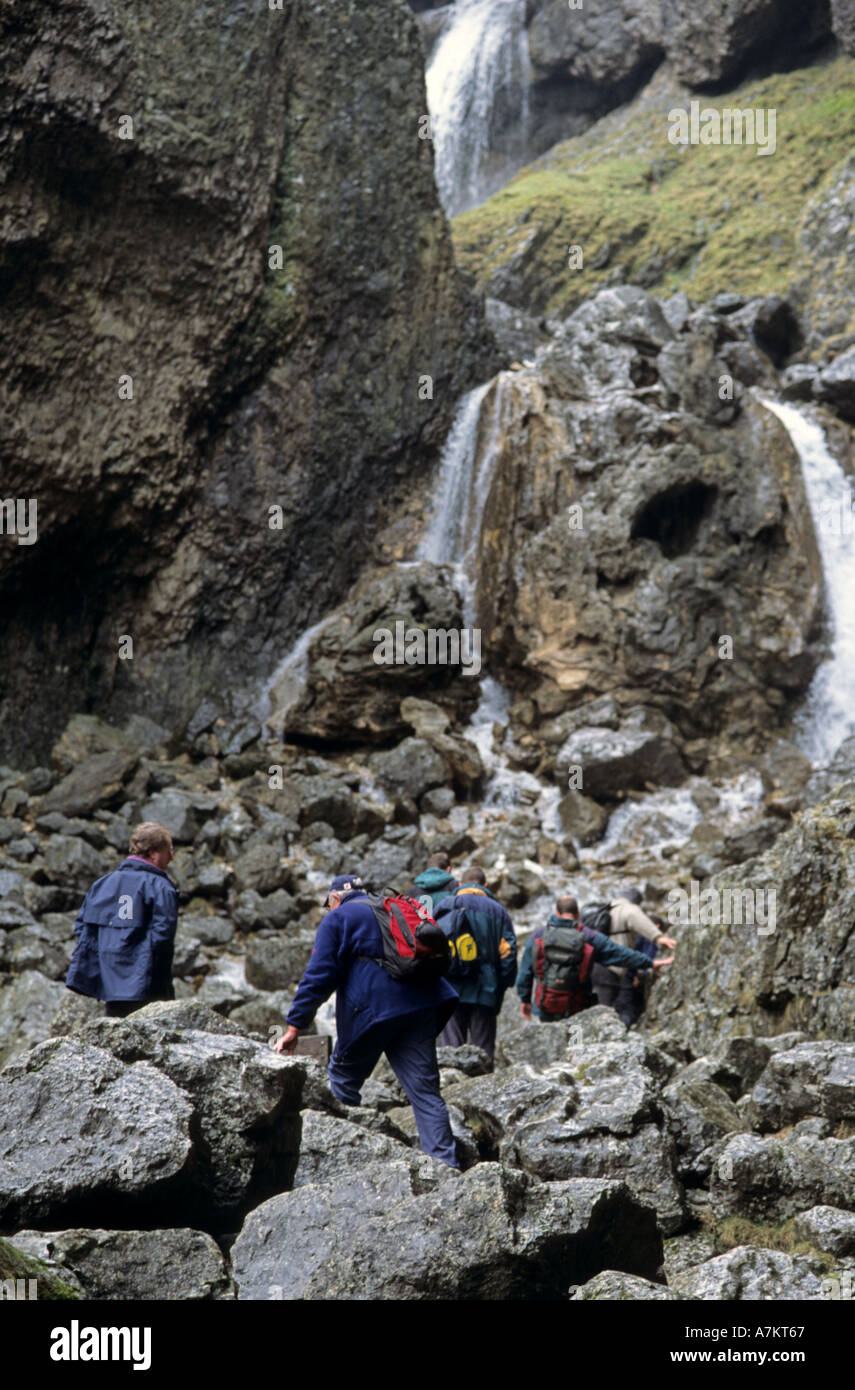 Walkers trek attraverso il lakedistrict inglese e salire una caduta dell'acqua. Wet scivolose rocce progredire difficile. Foto Stock