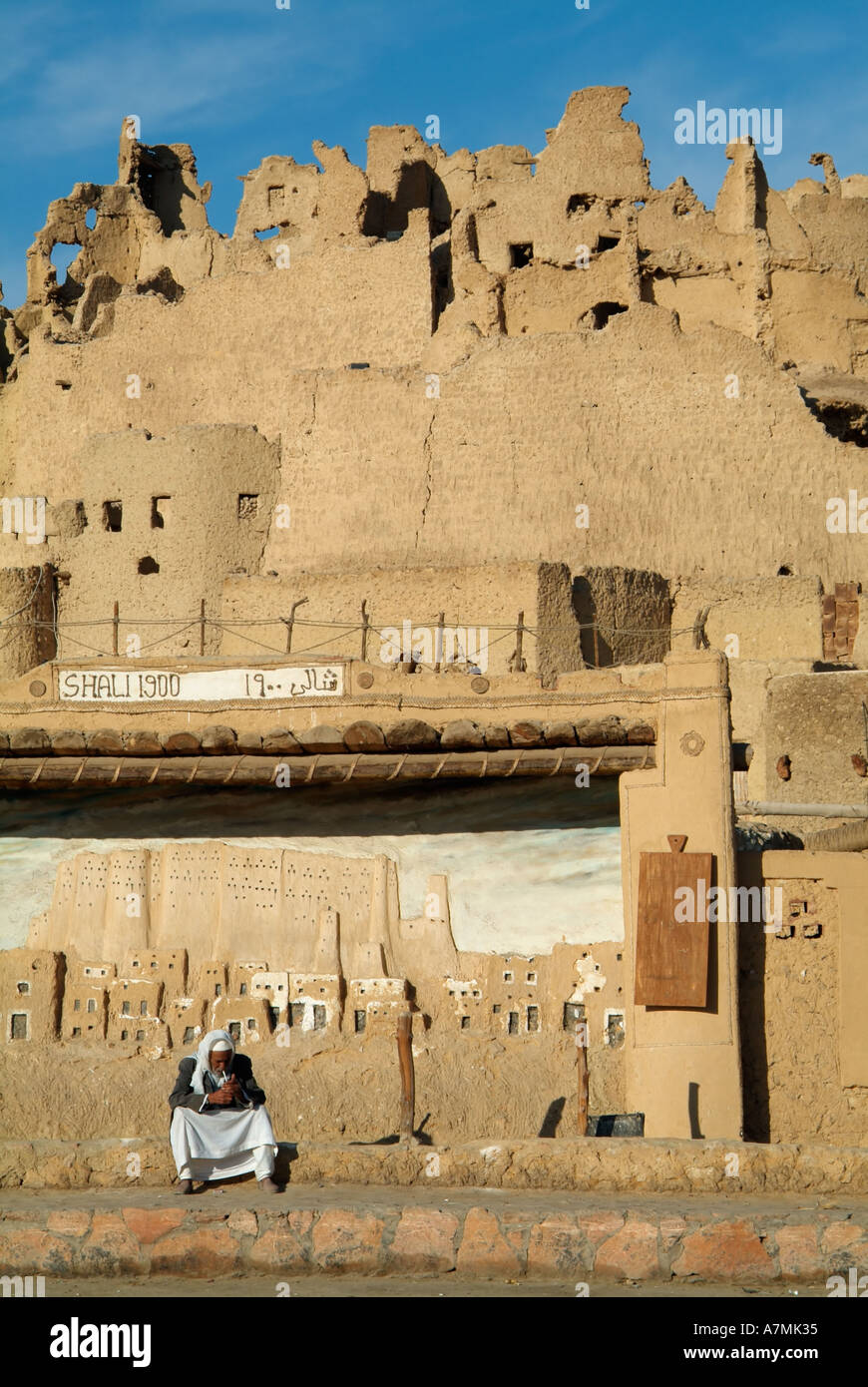 Egyptian uomo seduto di fronte a una placca per la città vecchia di Shali, Siwa, Egitto Foto Stock