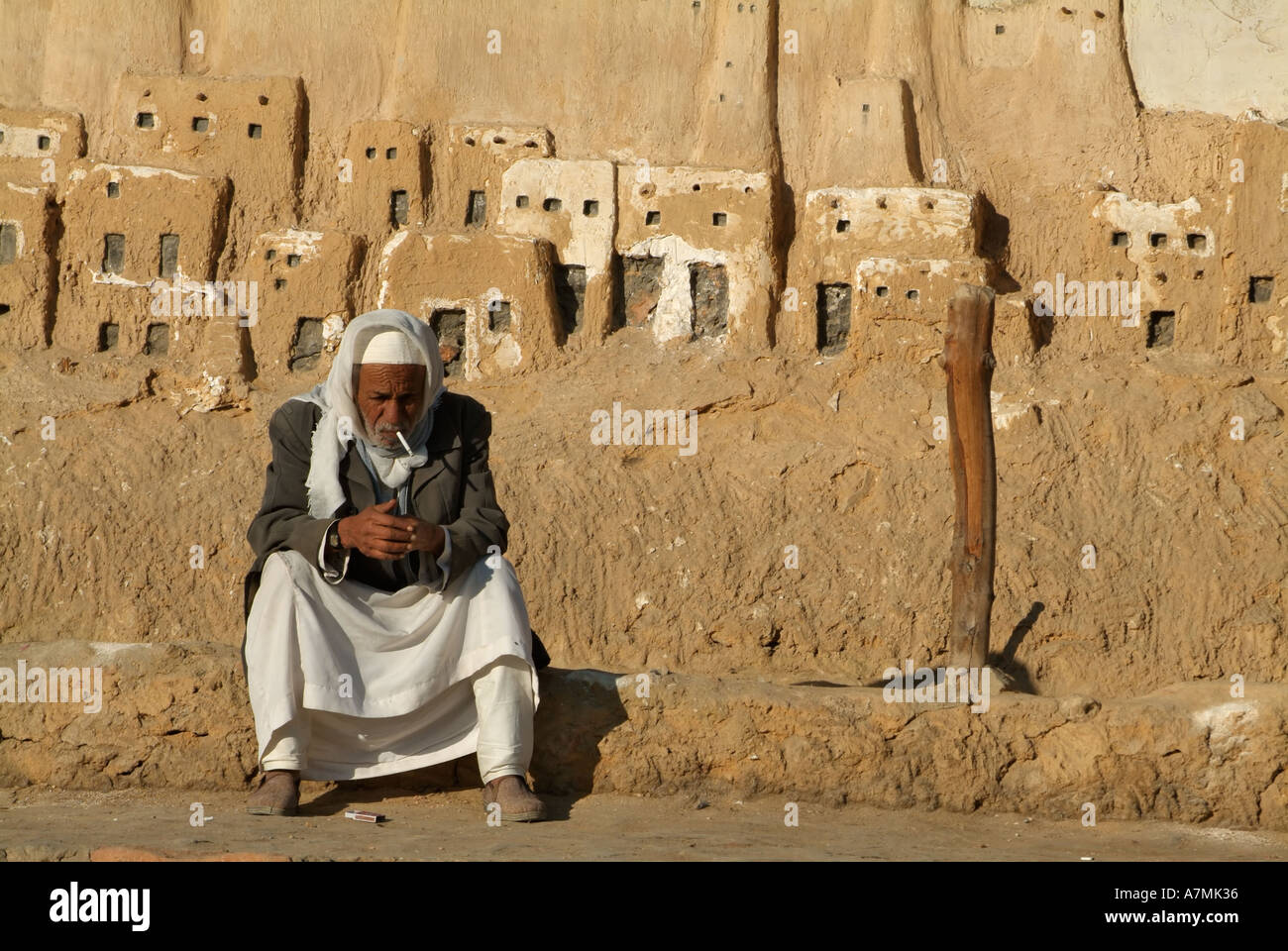 Egyptian uomo seduto di fronte a una placca per la città vecchia di Shali, Siwa, Egitto Foto Stock