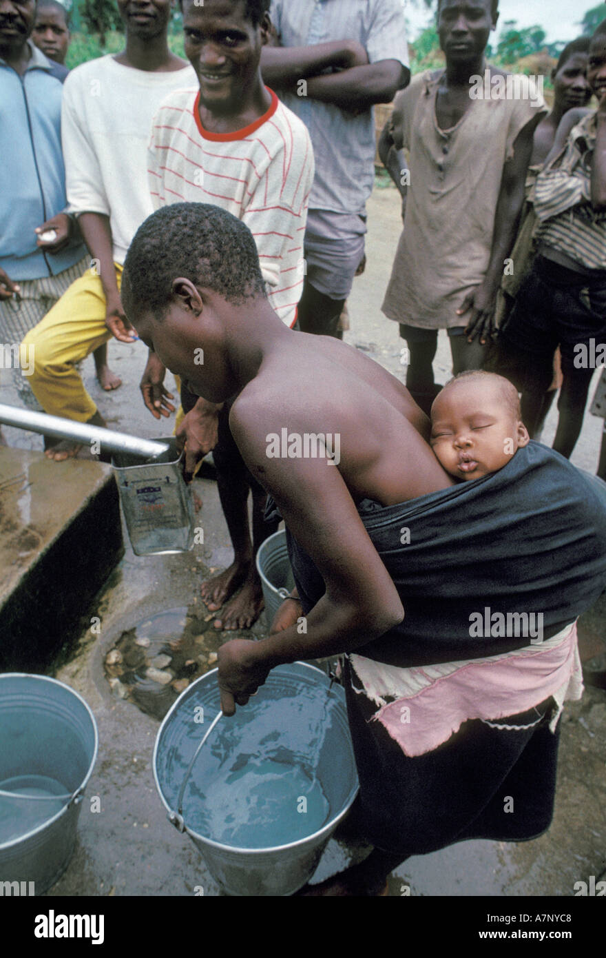 Vittime del conflitto una madre con bambino sulla schiena raccoglie acqua da ben guardato da uomini in Malawi Foto Stock