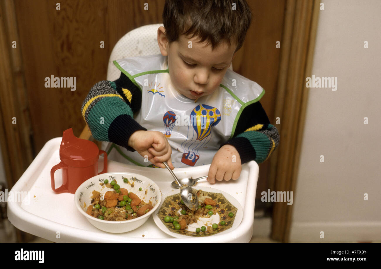 Due anni di bambino mangiare seduto in una sedia alta Foto Stock