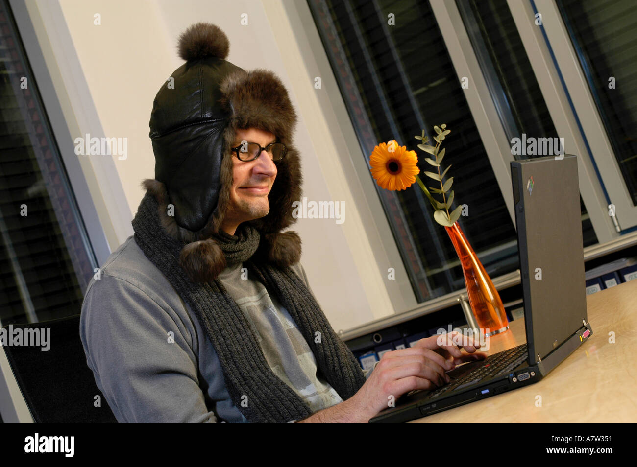 Uomo che lavora al computer portatile, indossando il cappuccio, sorridente Foto Stock