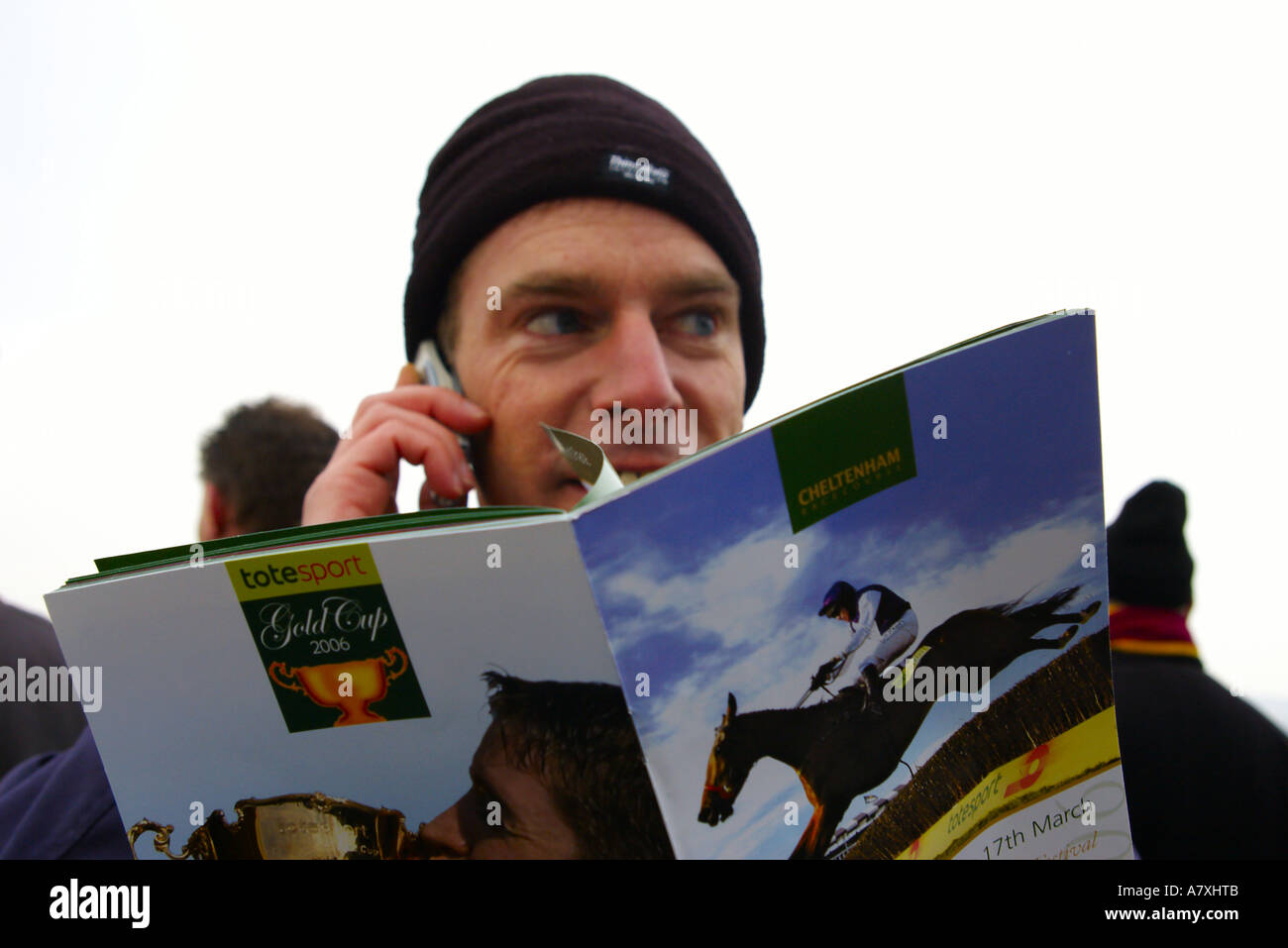Un clowning faccina felice l'uomo è utilizzando il suo mobile per scommettere denaro su corse di cavalli o corsa ad ostacoli a Cheltenham Gold Cup, gara corso Foto Stock