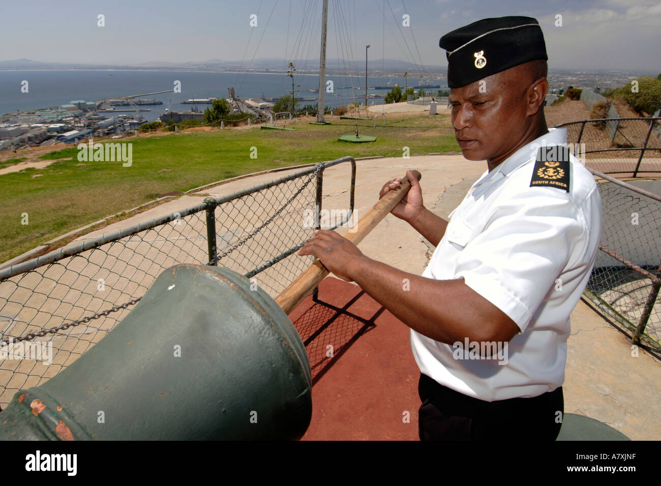 Chief Petty Officer Dudley malghe usando un cilindro di legno asta per spingere la carica nel muso del cannone di mezzogiorno il cannone a Cape Town. Foto Stock